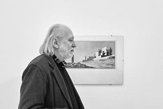black and white photo of hungarian author laszlo krasznahorkai standing in front of a painting