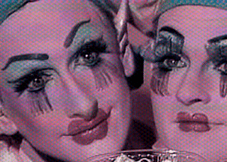 Two pink faces, painted like clowns with blue eyeshadow and caps, resting on a table, in a still taken from Tom Rubnitz's 1989 film strawberry shortcut