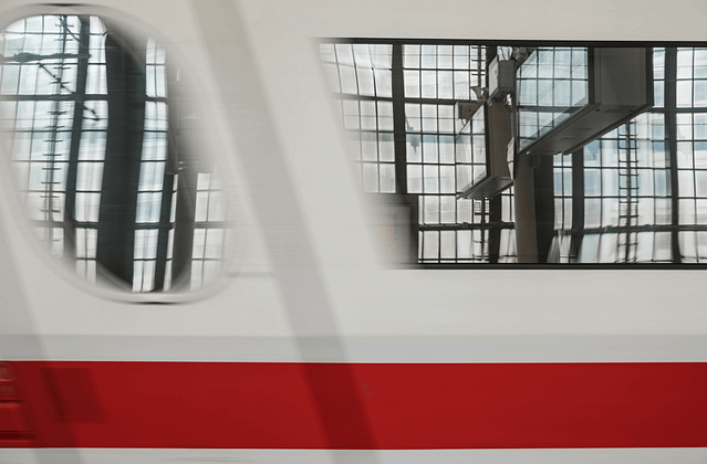 Close-up of a train’s windows as it is just beginning to leave the station. The station’s modern glass walls are reflected in the blur.