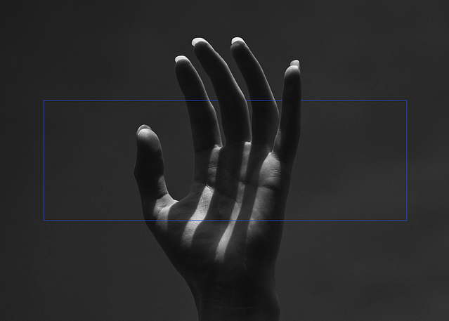 Black-and-white photograph of a hand reaching into the air. The outstretched fingers cast long shadows on the palm. The nails are long. A thin blue rectangular frame is overlayed on top of the hand, edited to appear as if weaving through the fingers.